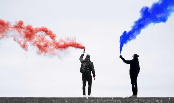 Dos jóvenes con aerosoles haciendo humear gases de color rojo y de color añil