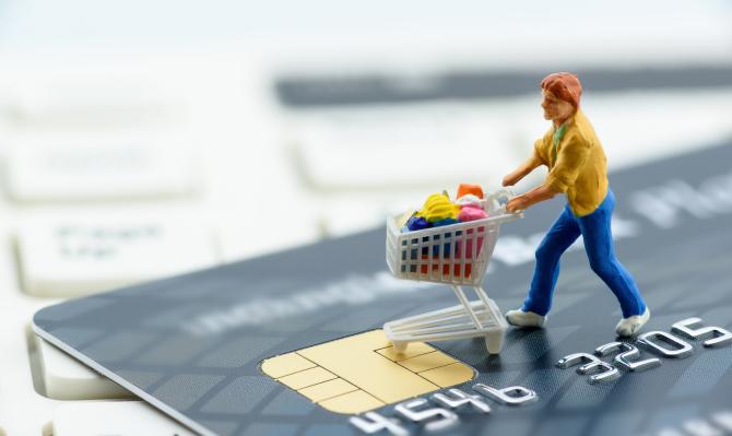 Figurita de mujer empujando un carrito de la compra sobre una tarjeta de crédito