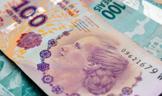 Billete de cien pesos argentinos sobre un billete de 100 reales brasileños