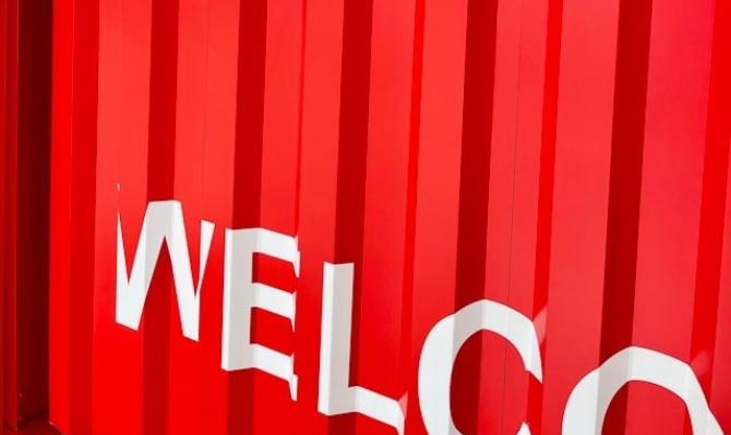 Contenedor de mercancías rojo con el rótulo "WELCO(ME)" en blanco. Photo by Andrii Leonov on Unsplash