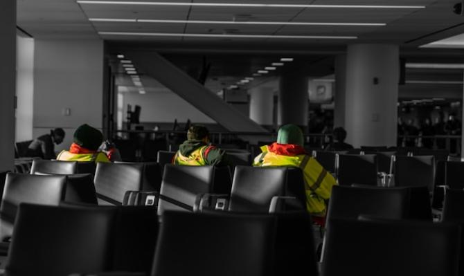 Tres trabajadores con chaleco reflectante sentados en la sala de espera de un aeropuerto. Photo by Austin on Unsplash