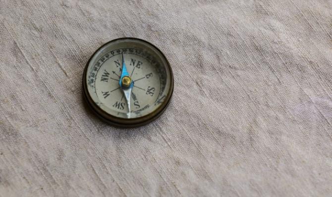 Brújula de latón señalando al norte sobre una tela blanca de lino. Photo by Mick Haupt on Unsplash