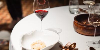 Mesa de restaurante con mantel blanco, copa de vino tinto, plato y cazuelilla de barro. Photo by Sander Traa on Unsplash