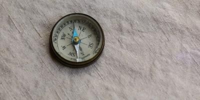 Brújula de latón señalando al norte sobre una tela blanca de lino. Photo by Mick Haupt on Unsplash