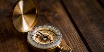 Brújula de bolsillo con tapa sobre madera oscura. Photo by Aaron Burden on Unsplash