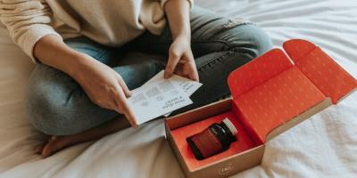 Mujer sentada en la cama abriendo una caja con un producto dentro para ilustrar un artículo sobre comercio electrónico de CaixaBank Research