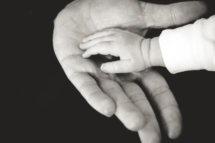 Mano adulta sosteniendo una mano de bebé sobre fondo negro