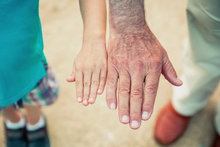 Mano de un niño pequeño al lado de la mano de un adulto de edad avanzada