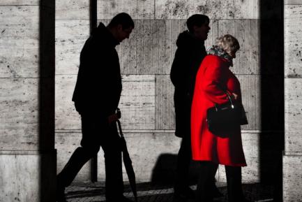 Joven, adulto y anciana con abrigo rojo caminando en un soportal