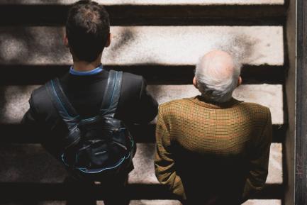 Joven y anciano de espaldas subiendo juntos unas escaleras
