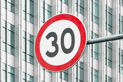 Señal de límite de velocidad a 30 frente a un rascacielos. Photo by Tinky on Unsplash