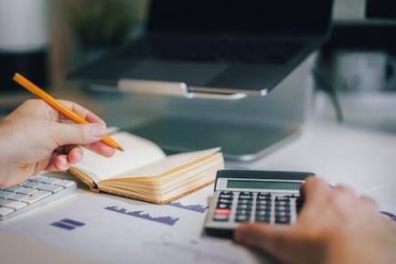 Hombre sujetando una calculadora y un bolígrafo en frente de un ordenador portátiol. Photo by Jakub Zerdzicki on Unsplash