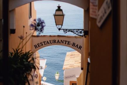 Callejuela de un pueblo marítimo con el mar de fondo y con carteles de "restaurante" para ilustrar el análisis económico de CaixaBank Research sobre el sector turístico y la restauración en España