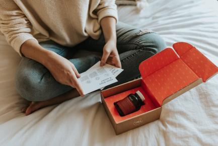 Mujer sentada en la cama abriendo una caja con un producto dentro para ilustrar un artículo sobre comercio electrónico de CaixaBank Research