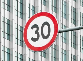 Señal de límite de velocidad a 30 frente a un rascacielos. Photo by Tinky on Unsplash