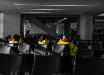 Tres trabajadores con chaleco reflectante sentados en la sala de espera de un aeropuerto. Photo by Austin on Unsplash