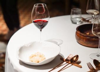 Mesa de restaurante con mantel blanco, copa de vino tinto, plato y cazuelilla de barro. Photo by Sander Traa on Unsplash