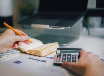 Hombre sujetando una calculadora y un bolígrafo en frente de un ordenador portátiol. Photo by Jakub Zerdzicki on Unsplash