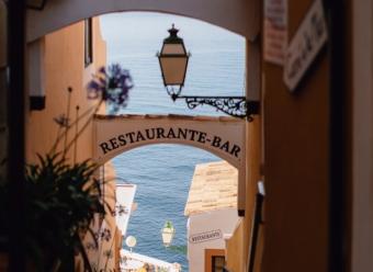 Callejuela de un pueblo marítimo con el mar de fondo y con carteles de "restaurante" para ilustrar el análisis económico de CaixaBank Research sobre el sector turístico y la restauración en España
