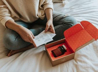 Mujer sentada en la cama abriendo una caja con un producto dentro para ilustrar un artículo sobre comercio electrónico de CaixaBank Research